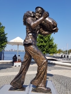 Bronze statue of a navy sailor at a coastal boardwalk location.