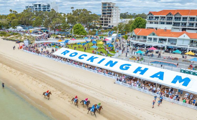 Horses on the beach running past a large Rockingham sign