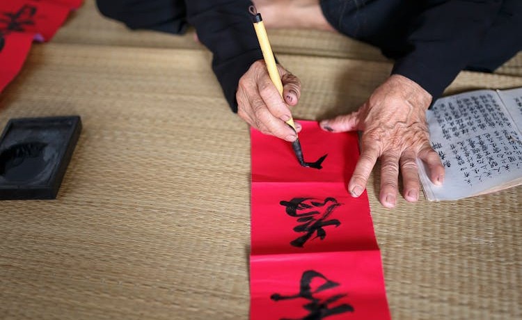 Person sitting with writing implement and red paper.