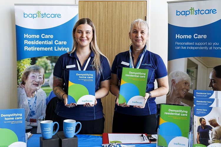 Two ladies standing at a BaptistCare display stand holding brochures.