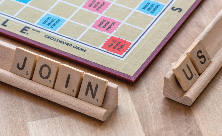 Scrabble tiles that spell Join Us in front of a scrabble board