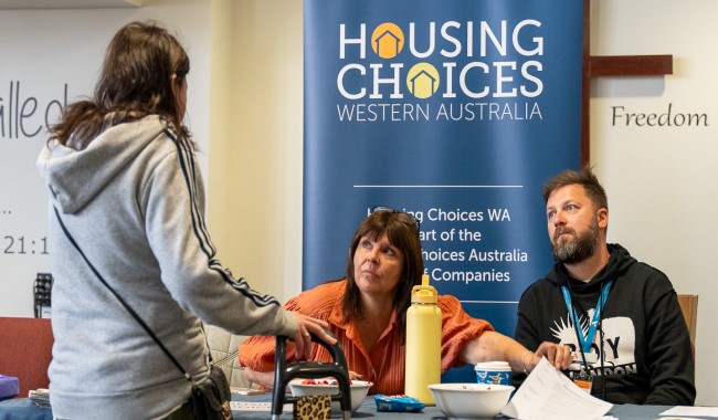 A person approaching two stallholders at an event seeking support regarding homelessness.
