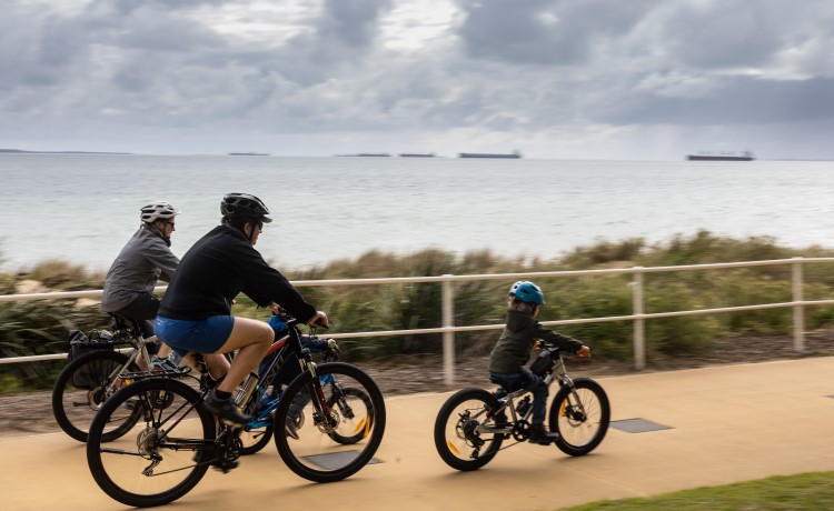 Young boy on bike and adults riding behind on the footpath adjacent to the beach
