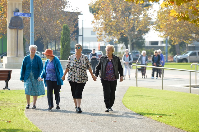 Four older women walking in a park and holding hands