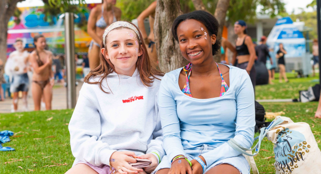 Two young people with face paint smiling sitting down at the Youth Beach Party 2025