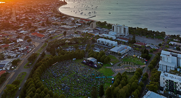 Aerial view of large community event in a park with the ocean in the background.
