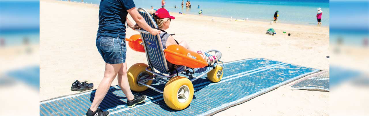 a beach wheel chair being pushed down some accessible beach matting