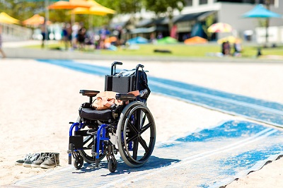 An empty wheelchair sits at the end of a stretch of blue beach access matting