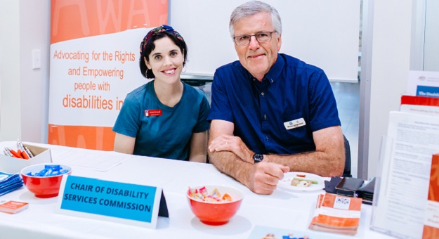 Two people sit at an information stall promoting the organisation People with Disability WA
