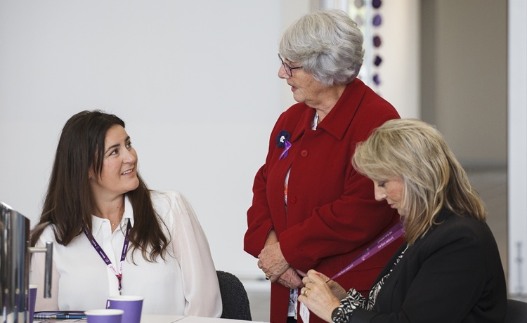 Having conversations about advanced care and planning. Two women sitting at a table, one standing and speaking.