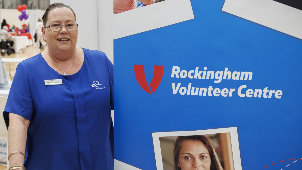 Smiling woman in a blue shirt standing in front of a blue banner for the Rockingham Volunteer Center