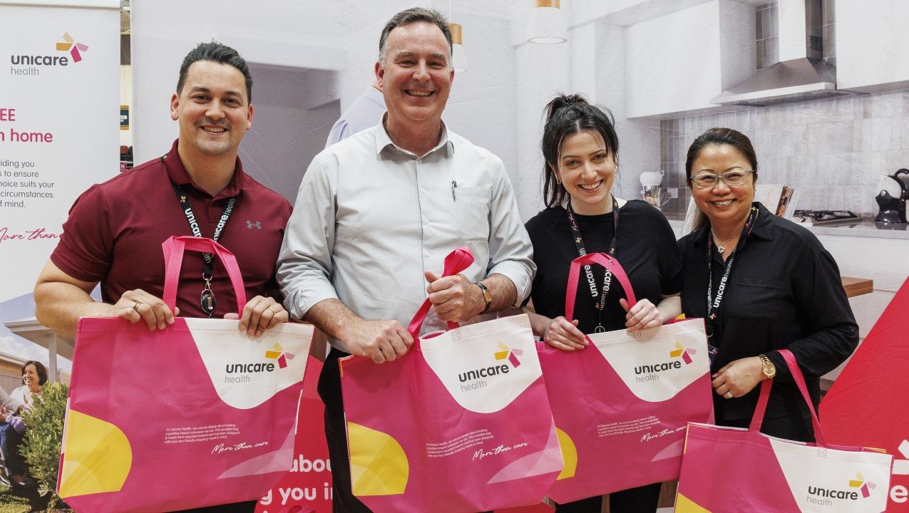 Two men and two women are smiling and holding up their pink bags with the Unicare logo on them.