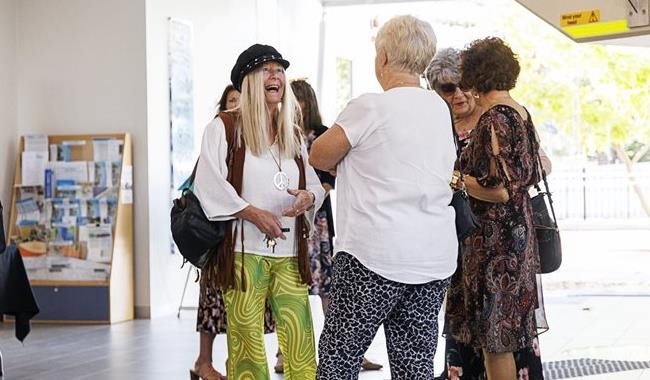 Several older people are standing and talking in the foyer of a community centre. One lady is laughing