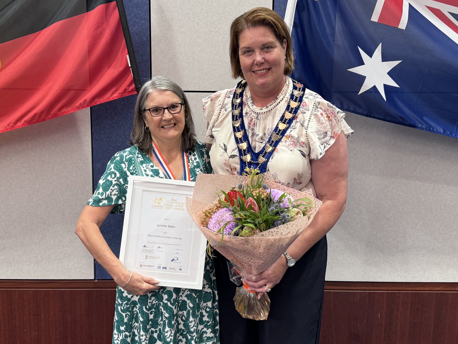 Gordon receiving his award from Mayor Deb Hamblin against a backdrop of a large Australian flag.
