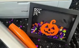 a black frame with a pumpkin and buttons on it next to a roll of vinyl
