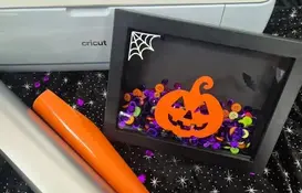 a black frame with a pumpkin and buttons on it next to a roll of vinyl