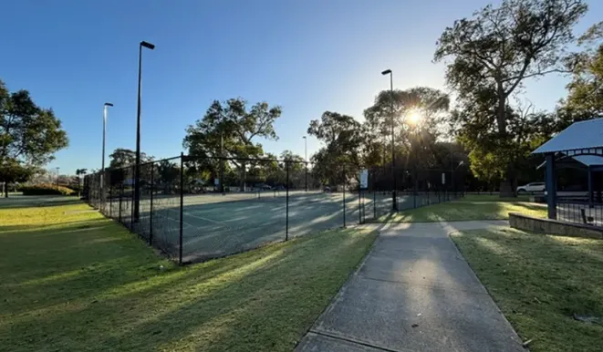 a tennis court with trees and a sidewalk