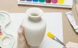 a hand holding a white vase with a yellow brush