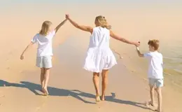 a woman and two children holding hands on a sandy beach