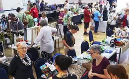 Busy indoor Christmas market with visitors browsing handmade crafts, gifts and artisan stalls.