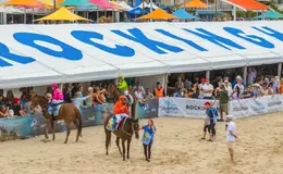 people riding horses on the beach in front of crowds