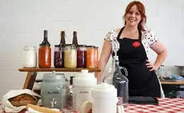 a woman standing behind a table with jars of food