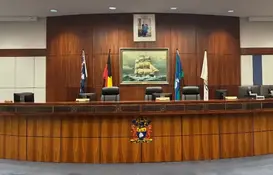 empty council chambers with warm lighting and a painting of a ship behind the bench. 