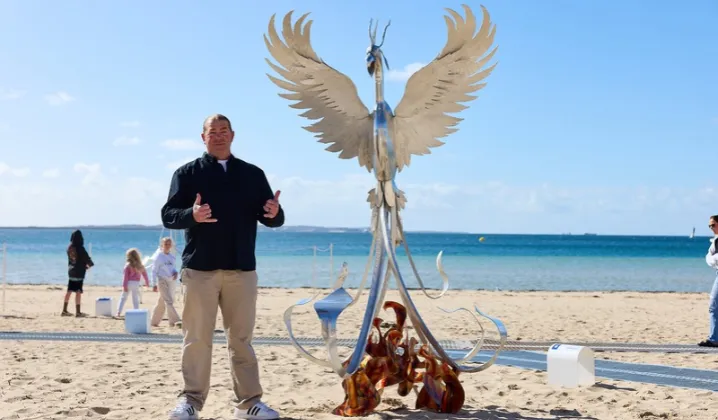 a man standing in front of a statue of a bird on a beach