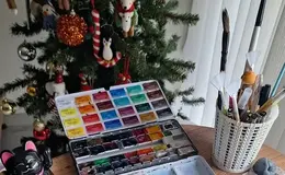 a paint box with paint brushes and a christmas tree