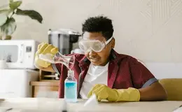 a person wearing safety goggles and gloves pouring liquid into a bottle
