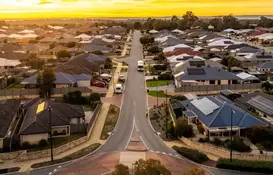 Aerial view of a suburban residential neighborhood at sunset, with a straight two-lane road running through the center. 