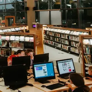 Interior of a library with bookshelves, computer stations and warm overhead lighting