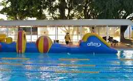 Large inflatable aqua obstacle course floating in an outdoor swimming pool.