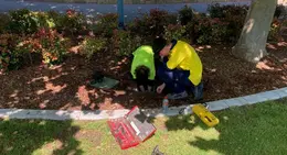 Two youth trainees working together on a maintenance task in a garden bed with tools laid out nearby.