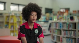 a boy with curly hair sitting in a room with books