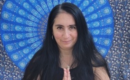 a woman with her hands together in front of a blue and white patterned fabric