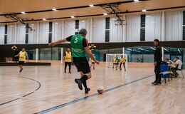 a man in a green shirt kicking a football ball on a wooden floor