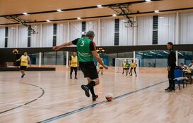 a man in a green shirt kicking a football ball on a wooden floor