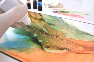 Close up of artist's hand creating an abstract artwork with alcohol ink.