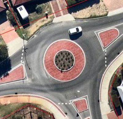 Overhead image of a suburban roundabout featuring red brick paving, pedestrian crossings, and central landscaping to enhance traffic flow and safety.